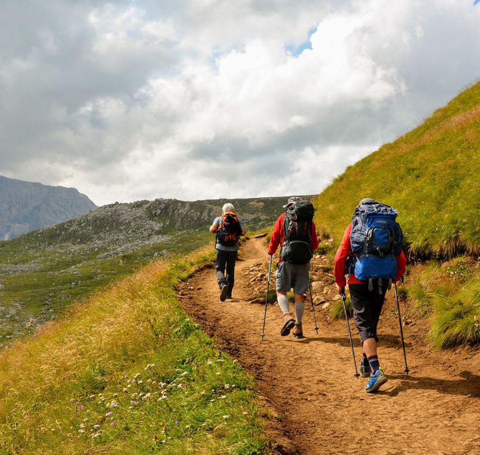 drei Personen mit Rucksäcken, die auf einem Wanderweg entlang wandern. 