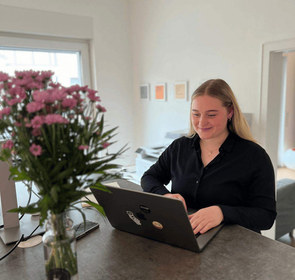 Person steht an einem Schreibtisch und hat einen Laptop vor sich.