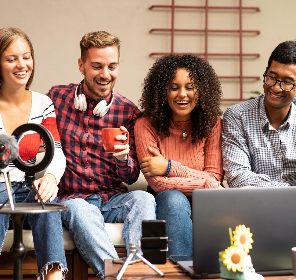 Vier junge Leute sitzen auf einer Couch und benutzen ein Handy und ein Laptop